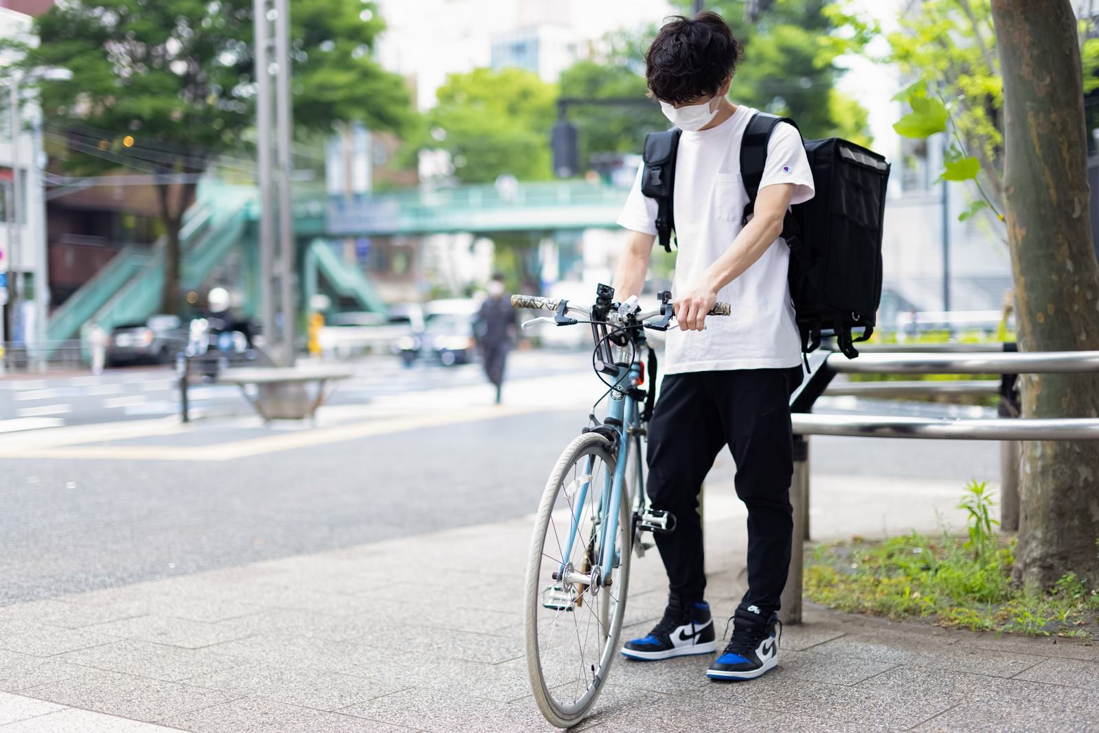 自転車の横でスマートフォンを見て配達先を確認するフードデリバリーの男性配達員［モデル：TSURUTAMA］