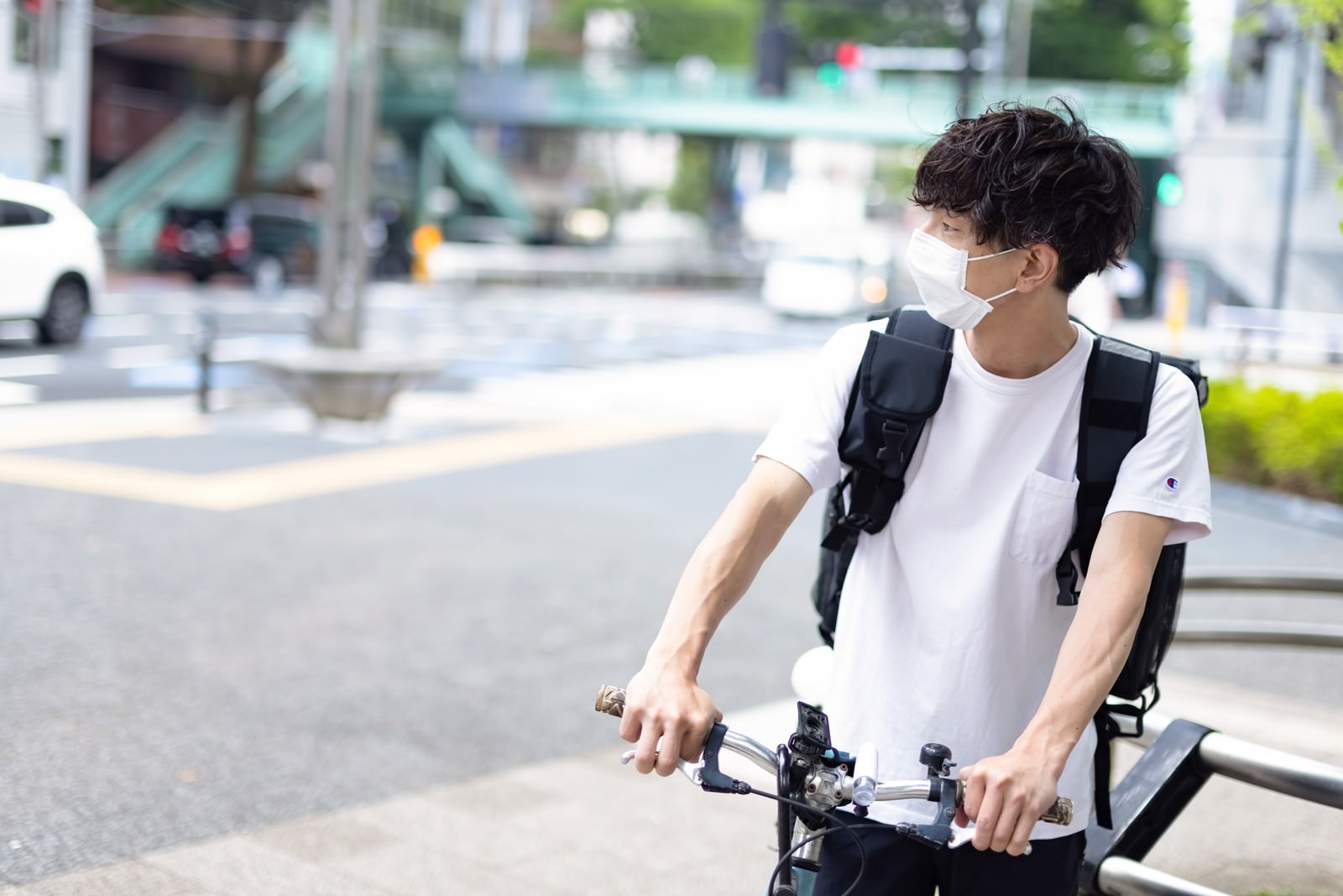 マスクを着用してリュックを背負い、自転車にまたがるフードデリバリー配達員の男性［モデル：TSURUTAMA］