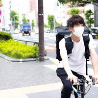 信号待ちをするフードデリバリーの配達男性の写真