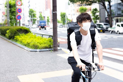 信号待ちをするフードデリバリーの配達男性