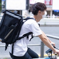 ウバッグを背負った男性配達員が自転車にまたがるの写真