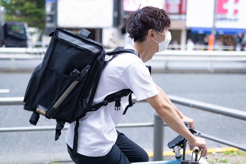ウバッグを背負った男性配達員が自転車にまたがる