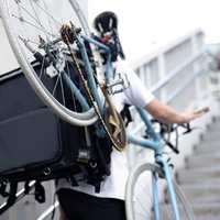 歩道橋の階段を自転車を背負って登る配達員の男性の写真