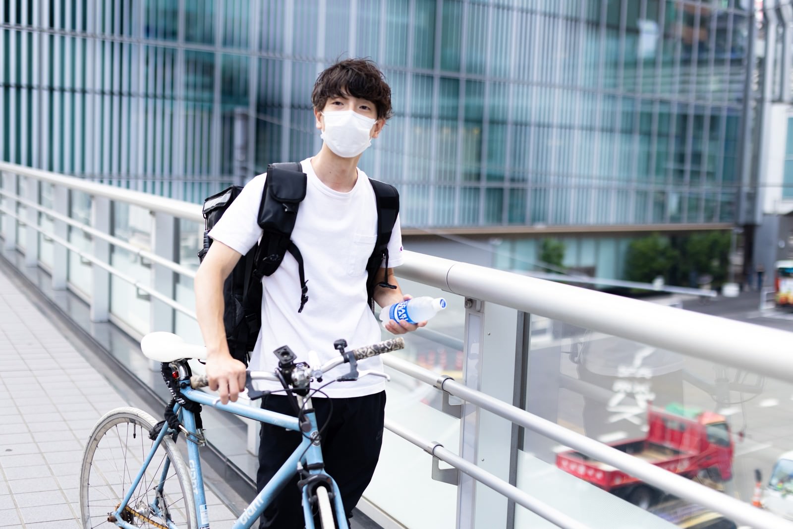 マスクをした配達員の男性が自転車と保温バッグを持って立っている