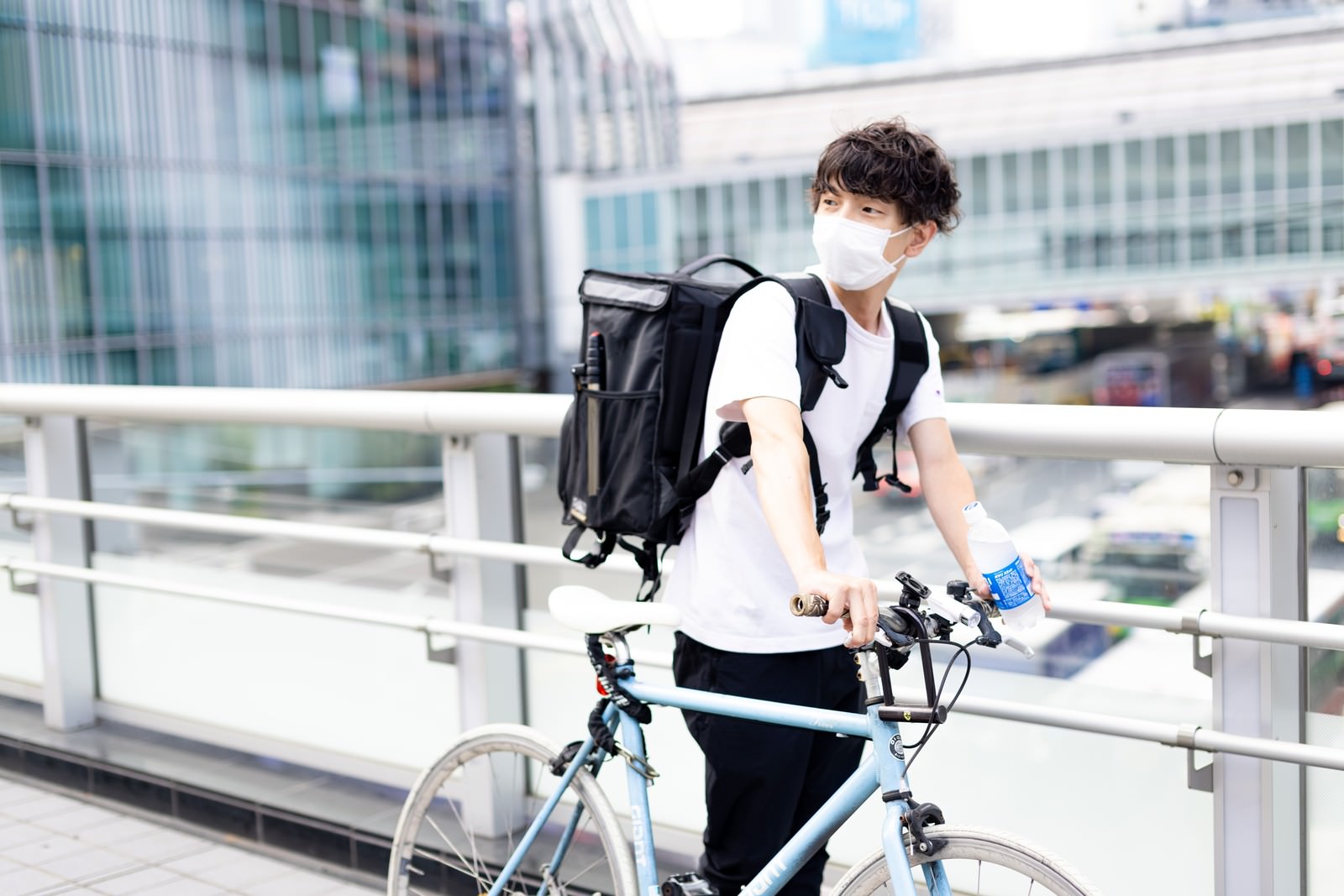 黒いリュックを背負い白い自転車を押して歩く配達員の男性［モデル：TSURUTAMA］