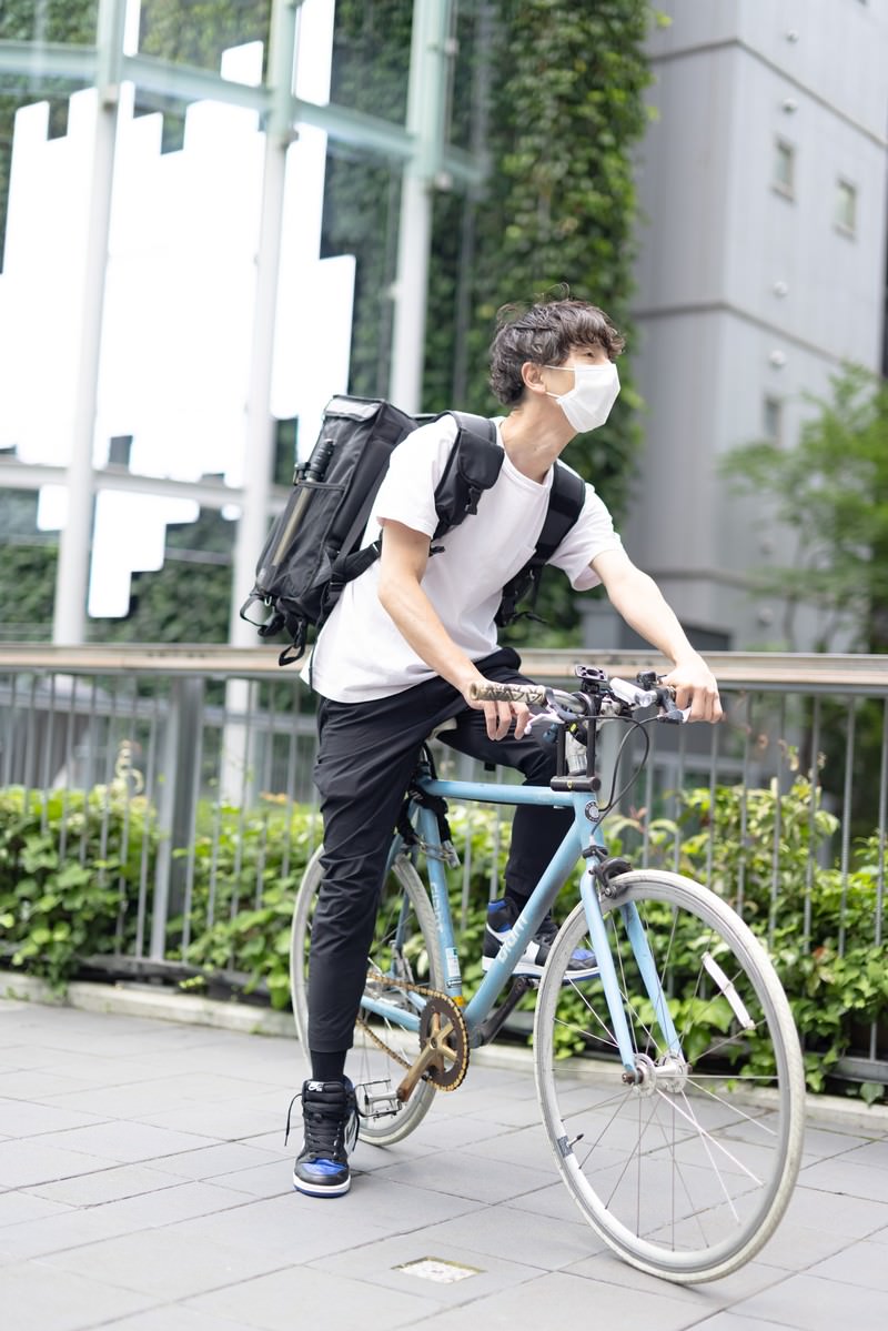 黒いリュックを背負って自転車にまたがる配達員の男性［モデル：TSURUTAMA］