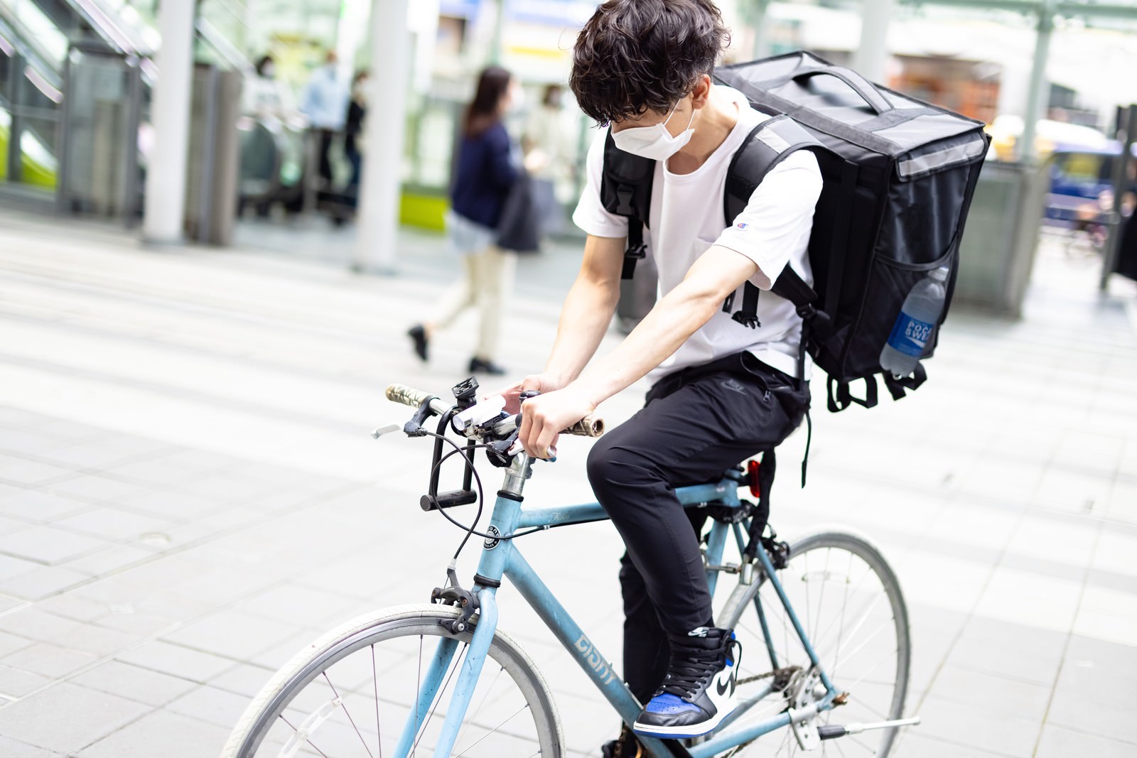 自転車にまたがりながら配達場所を端末でチェックするデリバリースタッフの男性［モデル：TSURUTAMA］