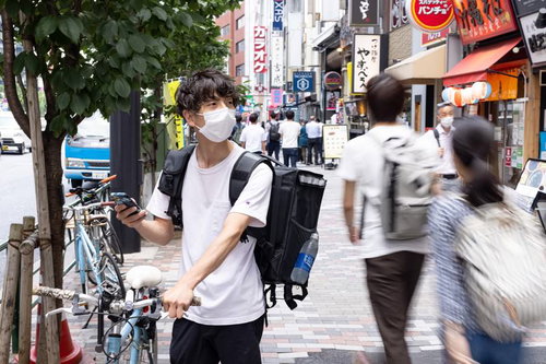 商品を受け取る店舗をスマートフォンで探す男性配達員