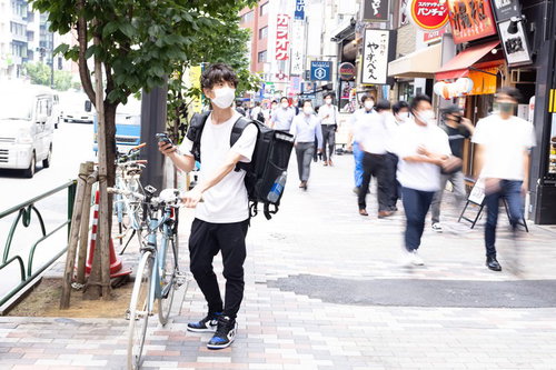 お昼時にフードデリバリーの配達依頼を受ける自転車配達員の男性