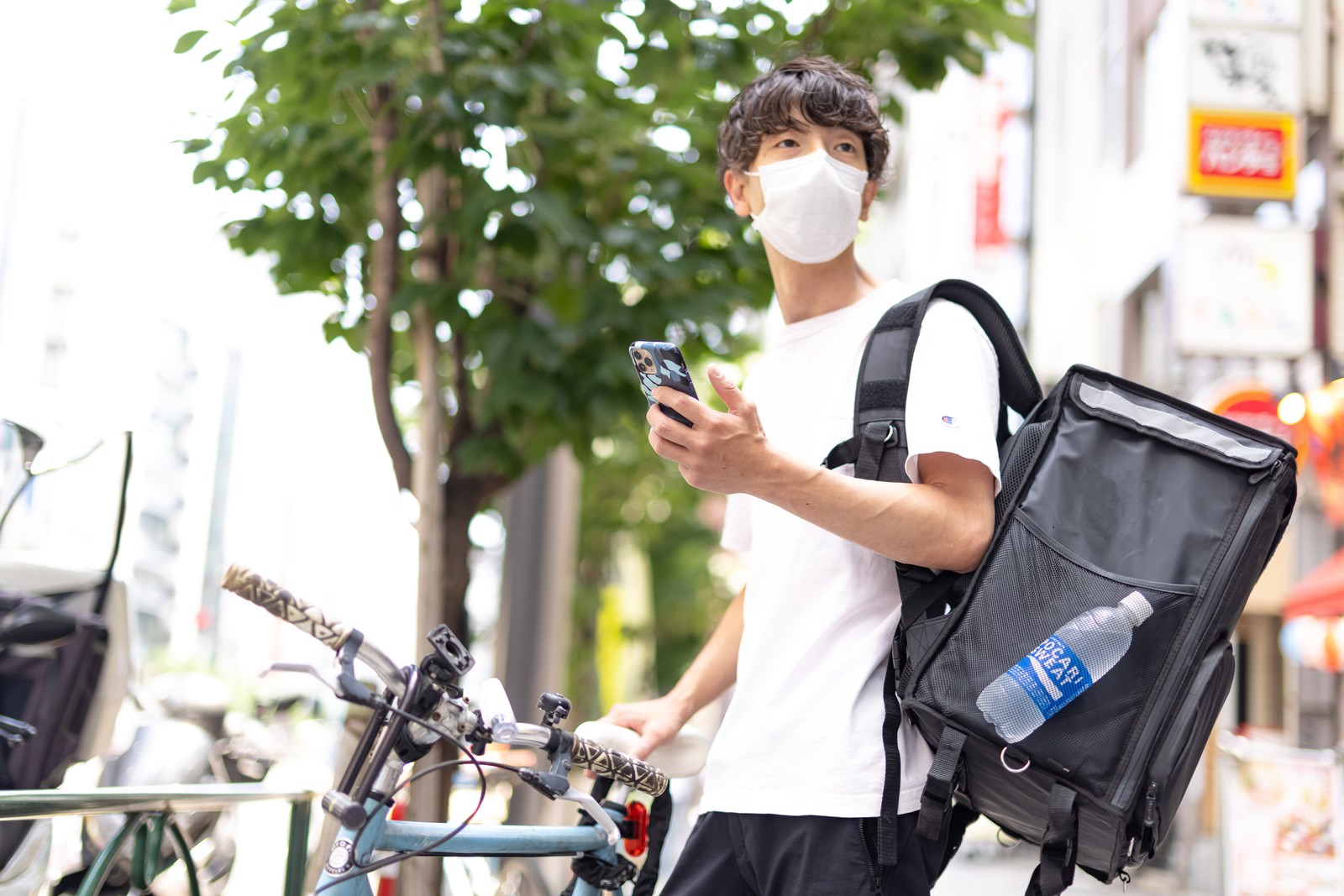 白いマスクを着用した配達員がスマートフォンの地図を見ている［モデル：TSURUTAMA］