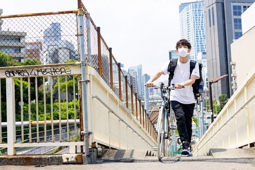 爽やかな配達パートナーが自転車で歩道橋を渡る