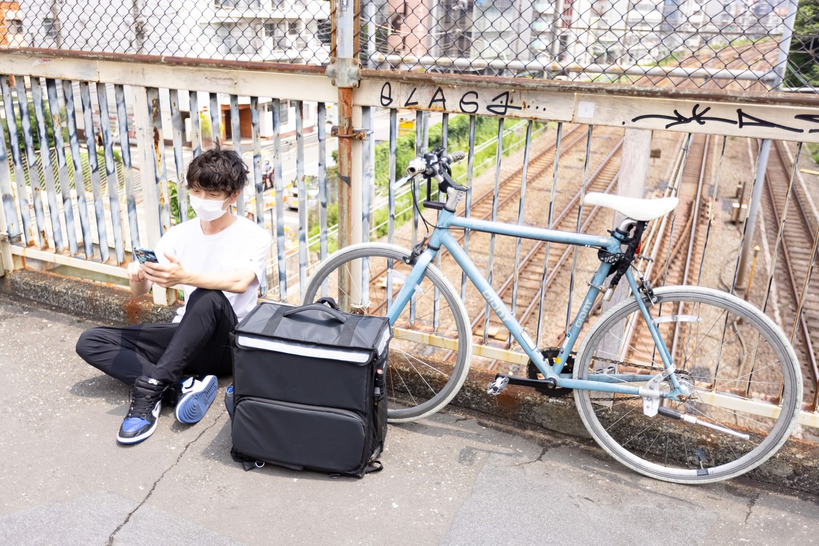 自転車の横に座り配達バッグを置いて休憩する男性配達員