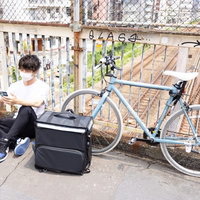 新しい依頼を待つ配達員と自転車、配達バッグでの休憩風景の写真