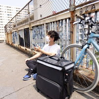配達合間に自転車の横で休憩する男性配達員の写真