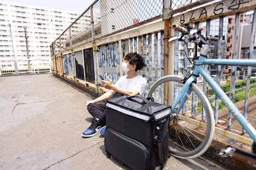配達合間に自転車の横で休憩する男性配達員