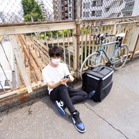 今日のノルマを達成して歩道の柵で休憩する配達パートナーの写真