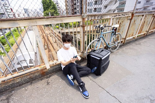 今日のノルマを達成して歩道の柵で休憩する配達パートナー