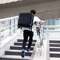階段を自転車を押して上る配達員の男性の配送業務の写真