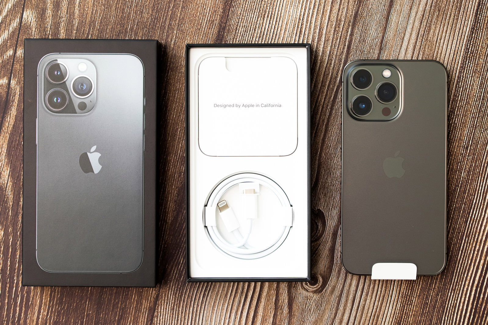 木目調のテーブルに置かれた開封済みのiPhone 13 Pro本体と化粧箱、ライトニングケーブル