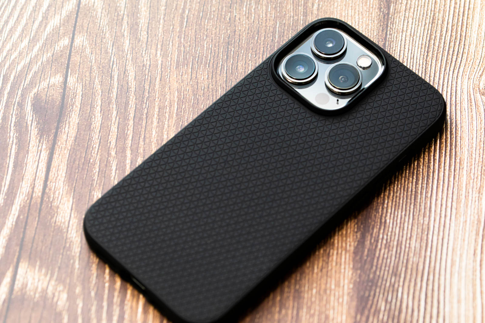 木目のテーブルの上に置かれた黒いスマホケースに入ったiPhone 13 Pro