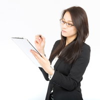 クリップボードとペンを持ちチェックする眼鏡の黒スーツの長い黒髪の女性の写真