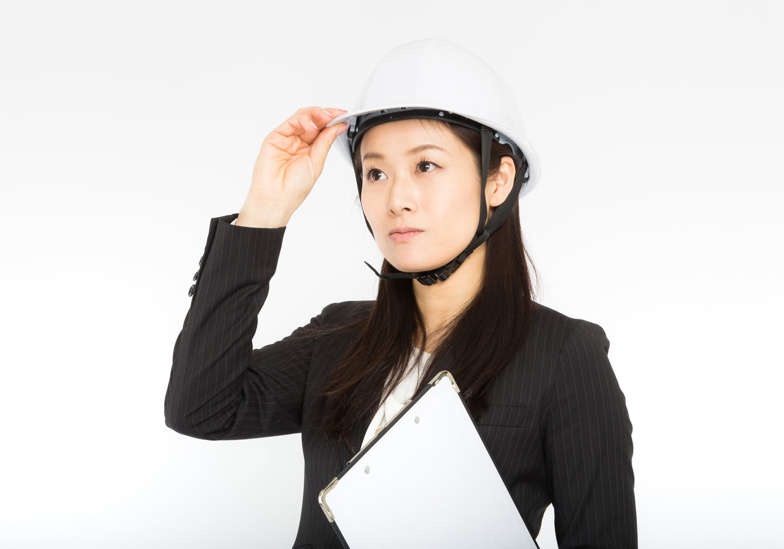 白いヘルメットを着用し、スーツ姿でつばを押さえる女性［モデル：土本寛子］