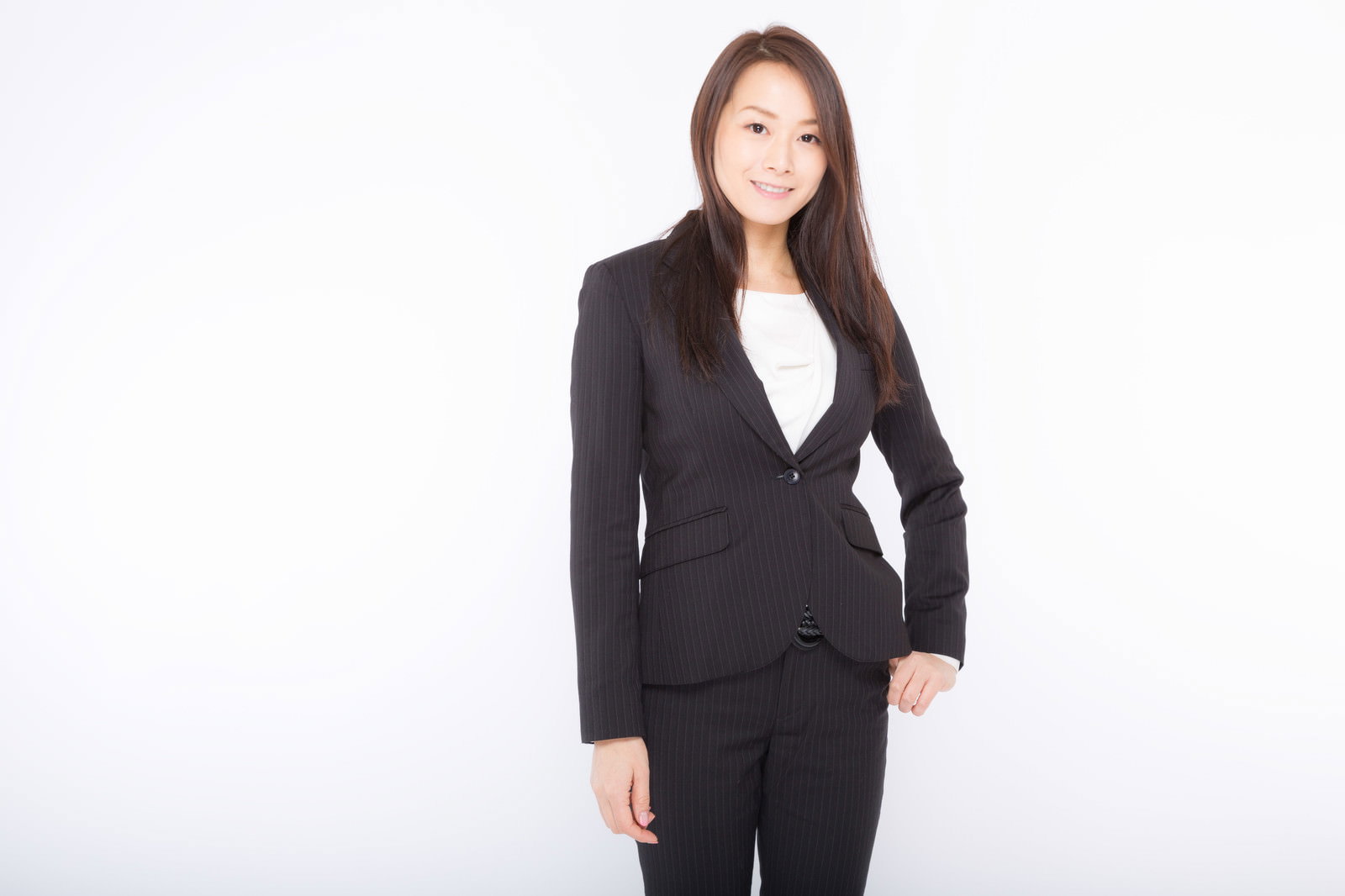 白い背景の前で黒いスーツを着て自信に満ちた表情を見せる女性［モデル：土本寛子］