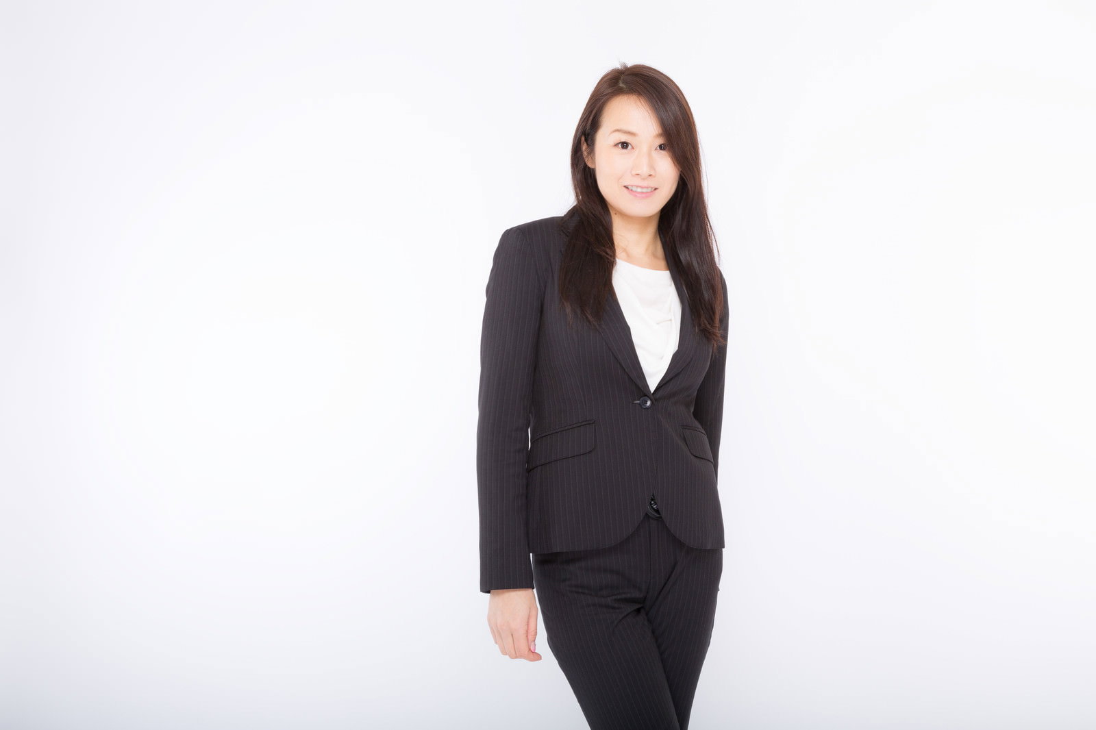 白背景の前で黒いスーツを着て立っている女性［モデル：土本寛子］