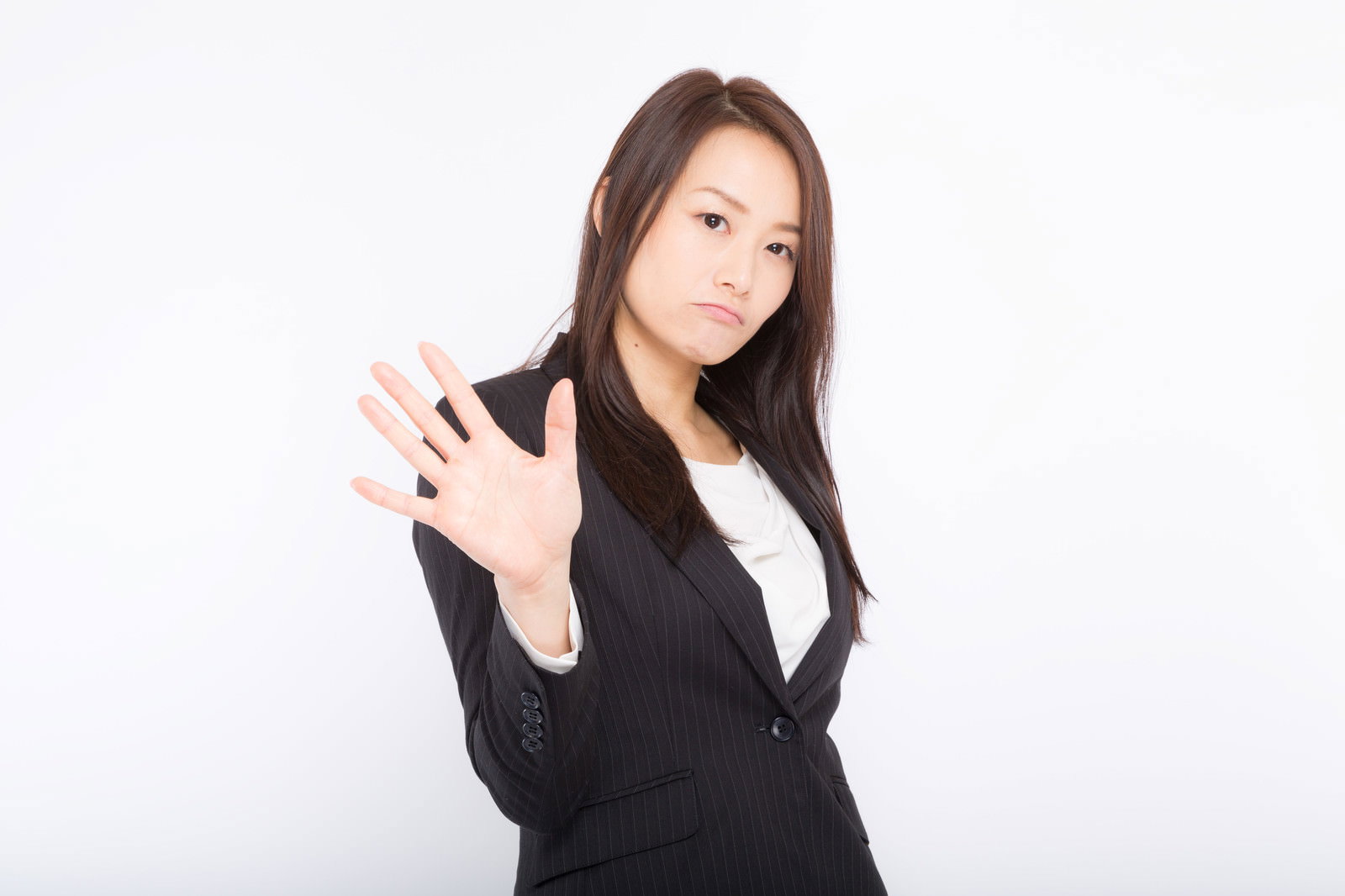 手を前に出して拒絶のポーズをとる黒いスーツの女性［モデル：土本寛子］