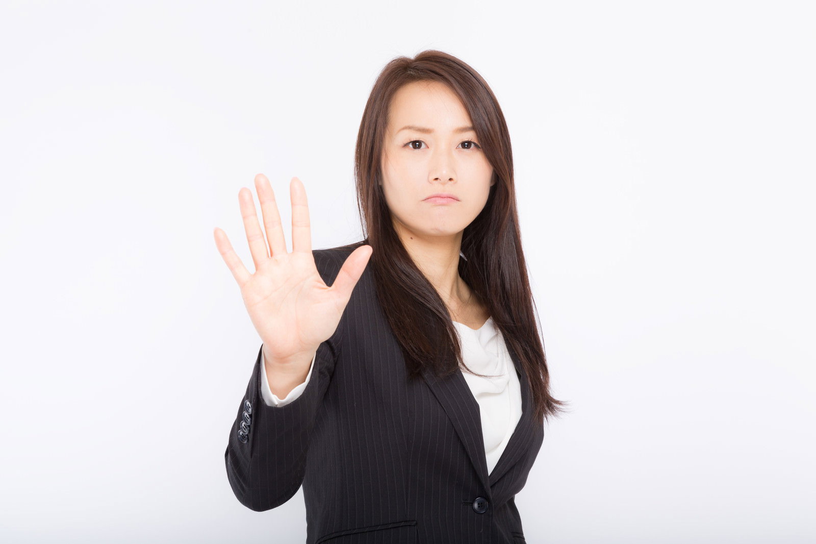 黒いスーツを着た女性が手のひらを前に向けて拒否のポーズをしている［モデル：土本寛子］