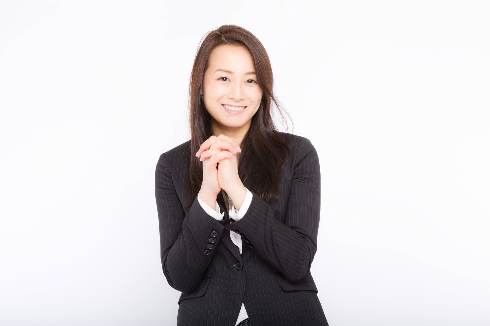 両手を合わせてお願いするポーズをとる黒いスーツ姿の女性従業員［モデル：土本寛子］