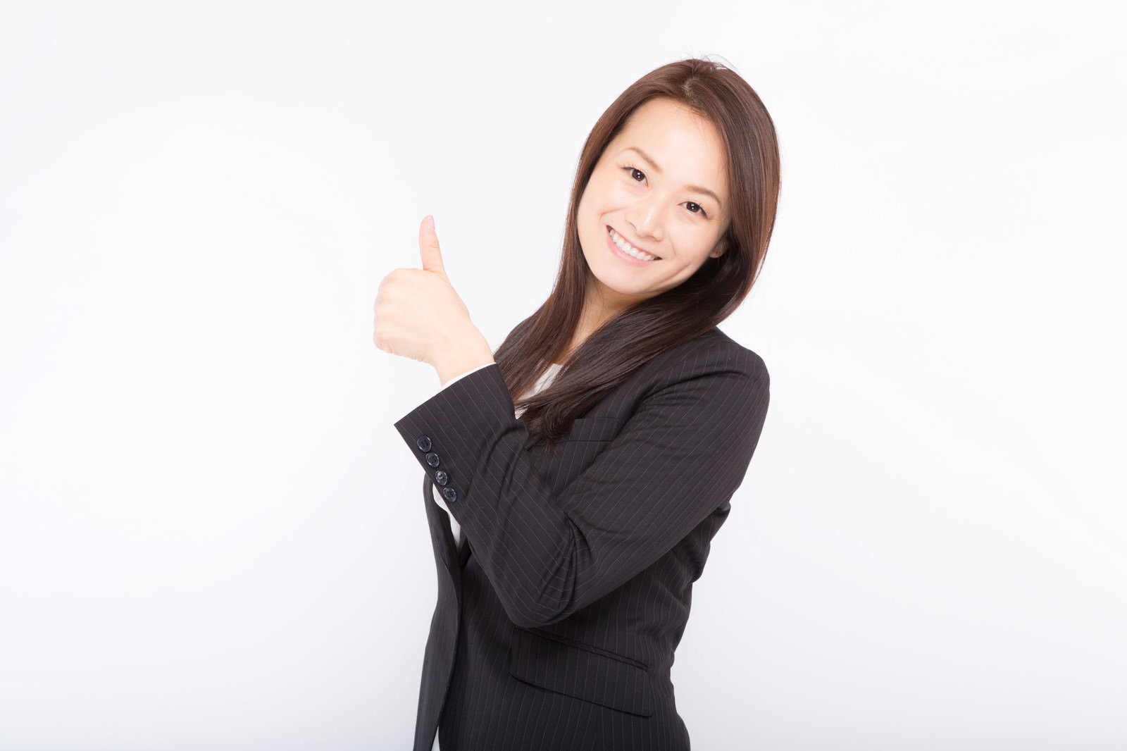 黒いスーツの女性が白背景で右手の親指を立てて笑顔でポーズをとっている［モデル：土本寛子］