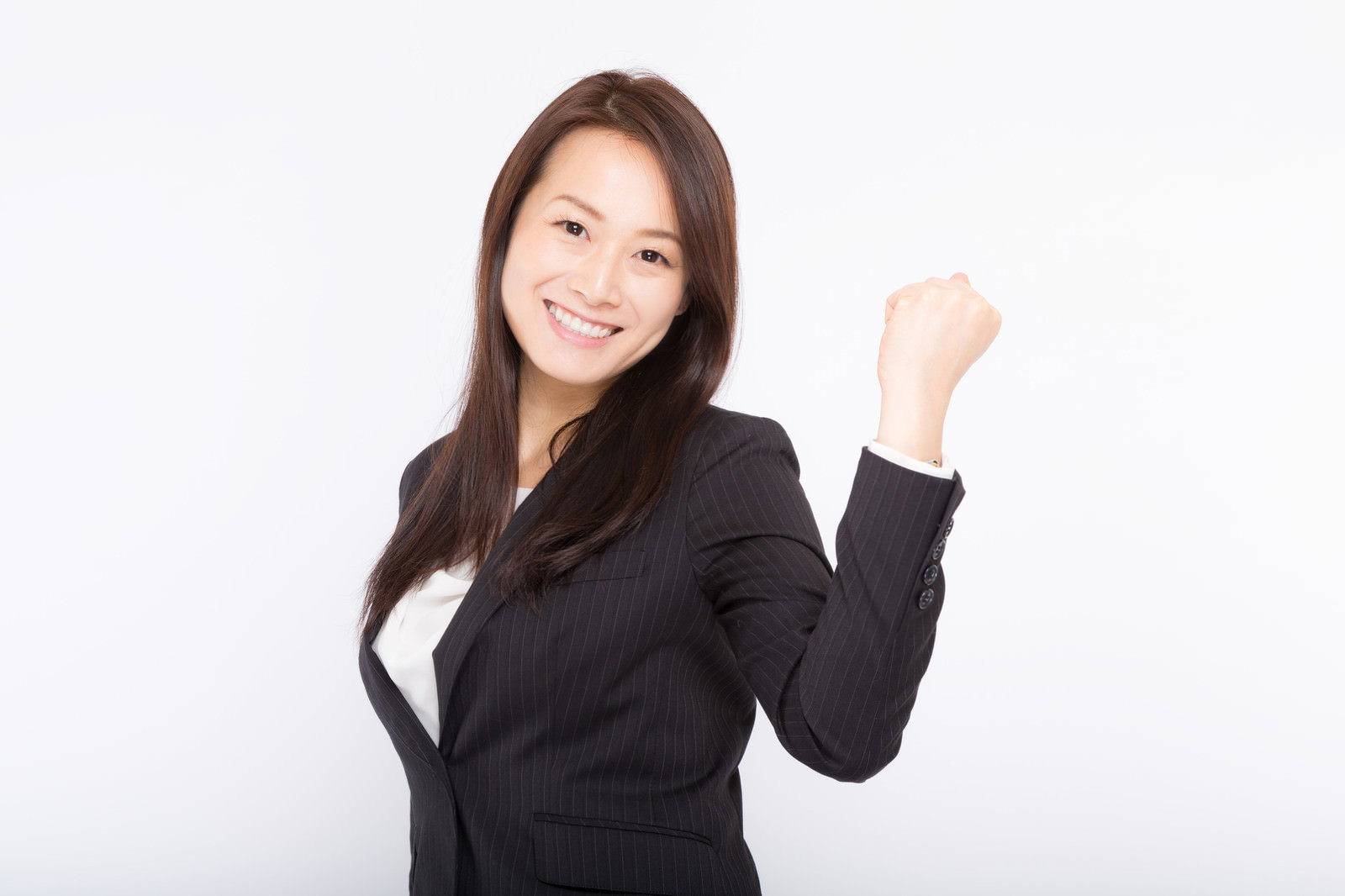 白い背景の前で右手を上げてガッツポーズをする笑顔の女性会社員［モデル：土本寛子］