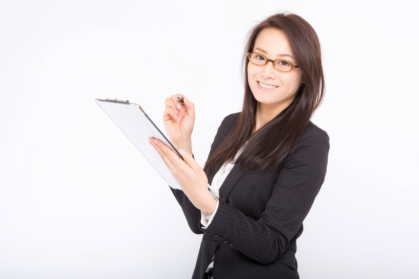 メモ帳を持ち笑顔でこちらを見つめるスーツ姿の女性社員［モデル：土本寛子］