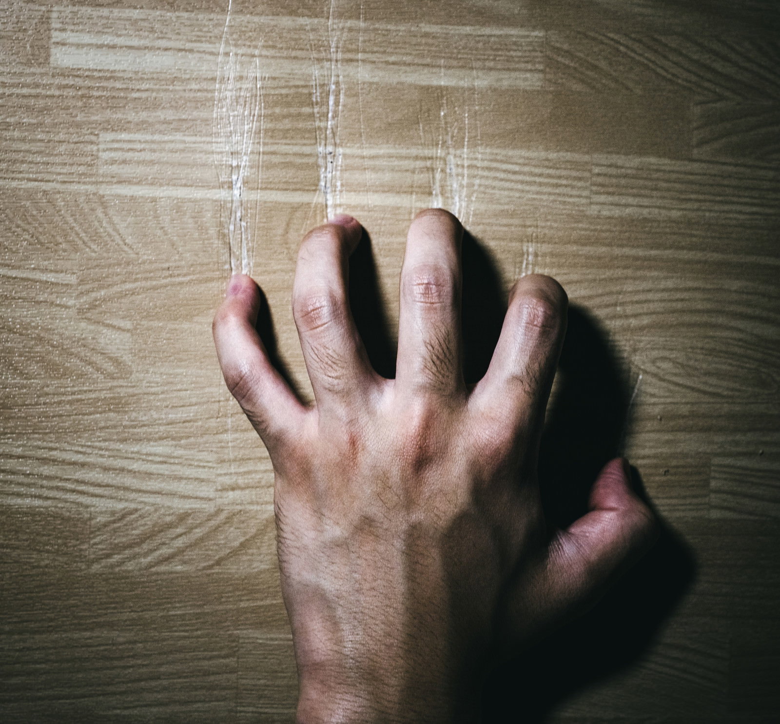 木目調の壁に手をついている人の手を撮影した写真