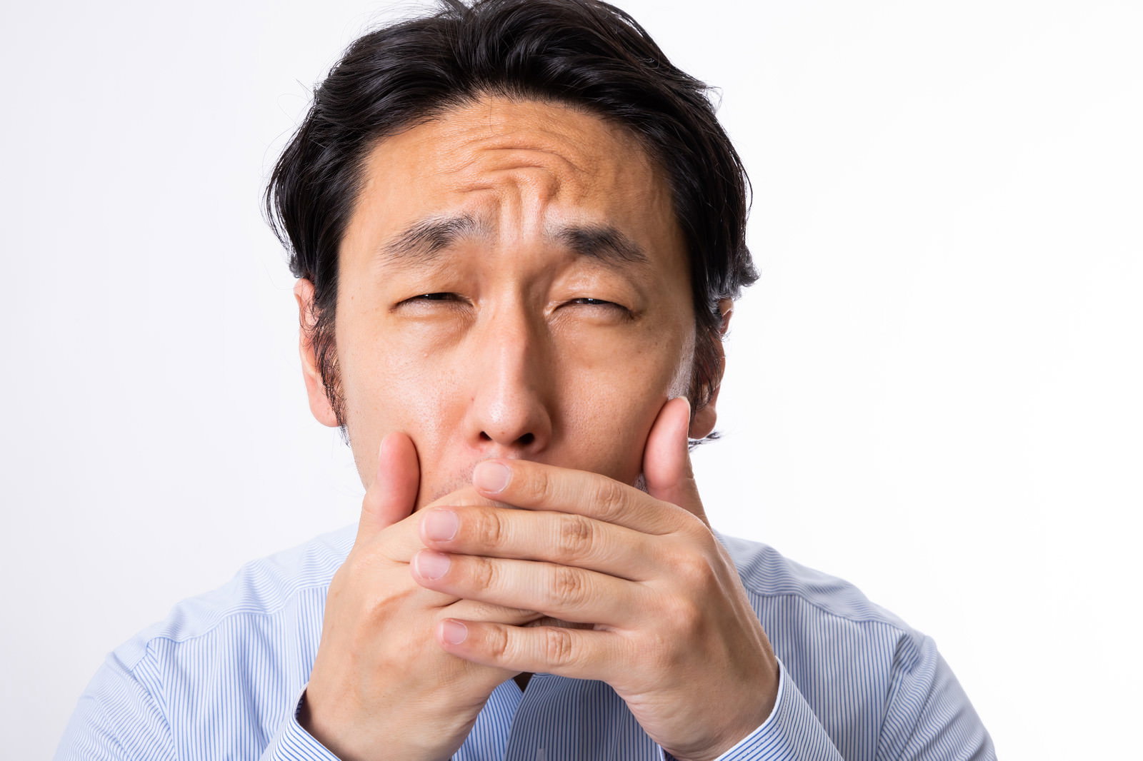 白いシャツを着た男性が両手で口元を覆い困った表情をしている［モデル：大川竜弥］