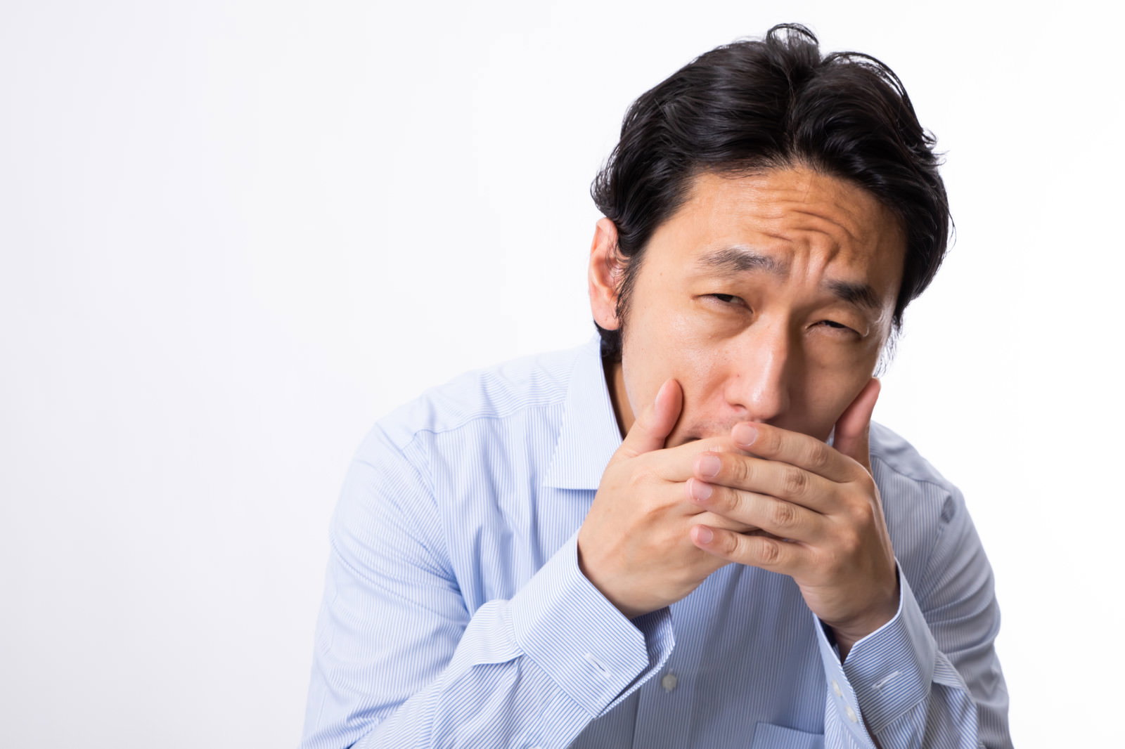 水色のシャツを着た男性が両手で口元を押さえて困った表情を見せている［モデル：大川竜弥］