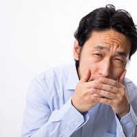 会議中にあくびをこらえて困った表情を見せる男性の写真