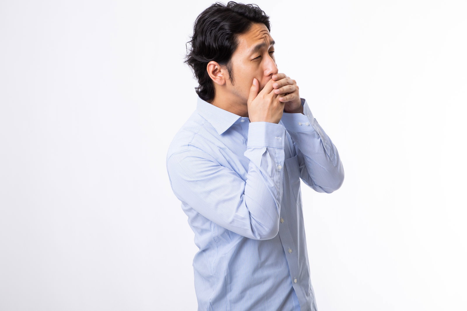 水色のシャツを着た男性が手で口を覆いながらあくびをしている［モデル：大川竜弥］
