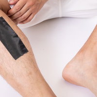 脱毛シートを毛深い足のすね毛に貼る男性のメンズ美容ケアの写真