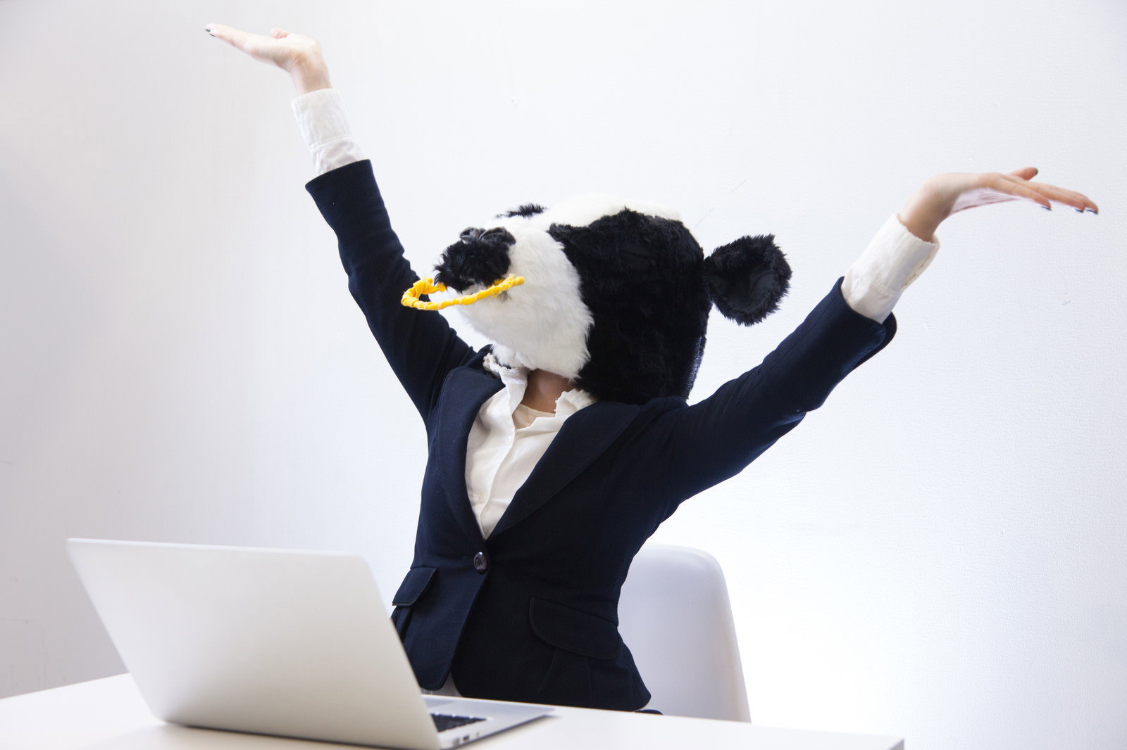 紺色ビジネススーツの牛キャラが両腕を高く上げ、黄色い王冠をかぶってオフィスで脱力している［モデル：古性のっち］