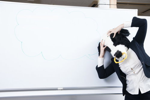 ホワイトボードの前で頭を抱えて困る牛女のビジネスイラスト