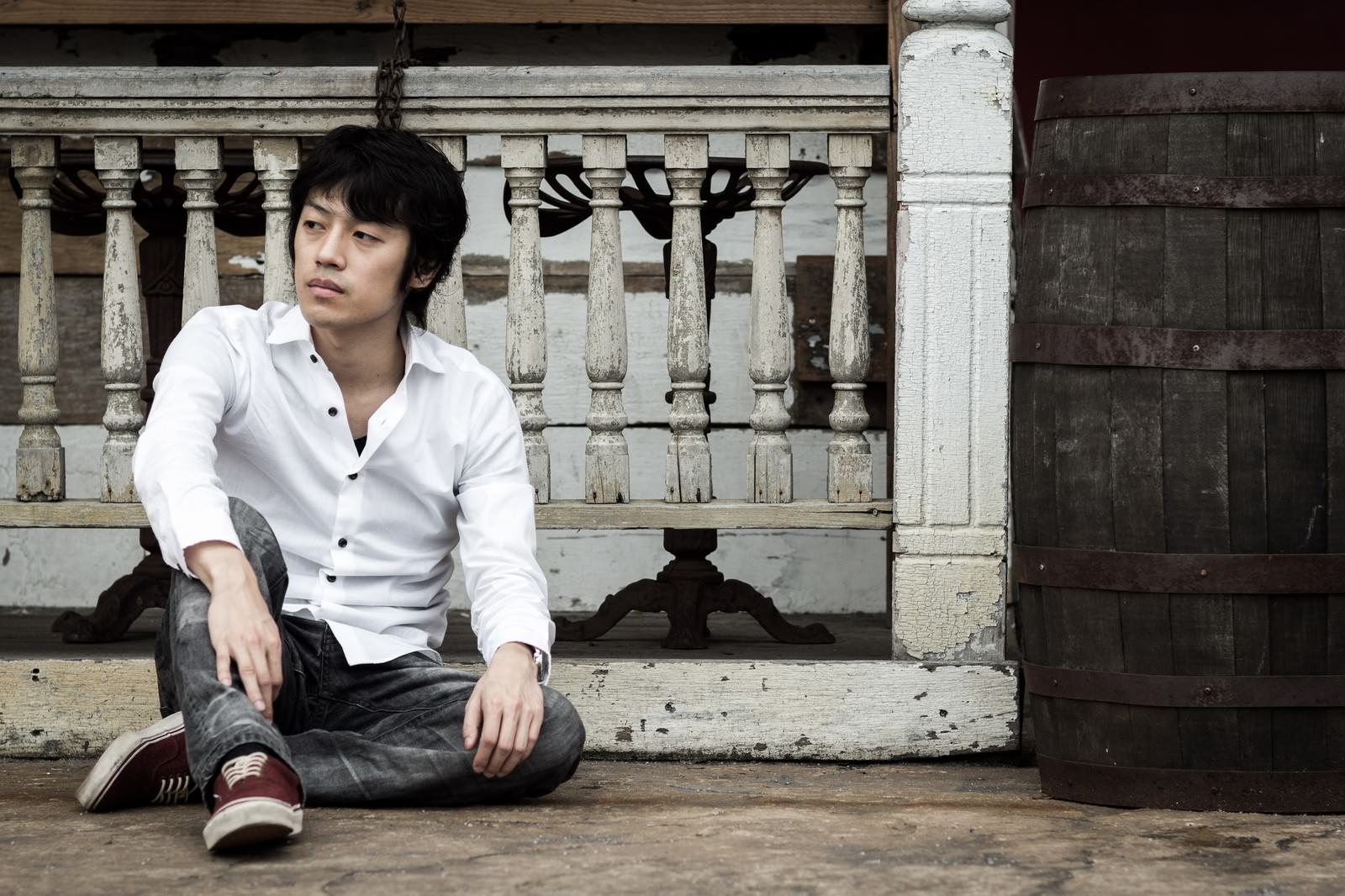 白いシャツを着た男性が古い洋館の前で疲れた表情で座り込んでいる［モデル：Tsuyoshi.］