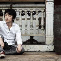 古い洋館の前で気だるそうに座り込む白いシャツの男性の写真