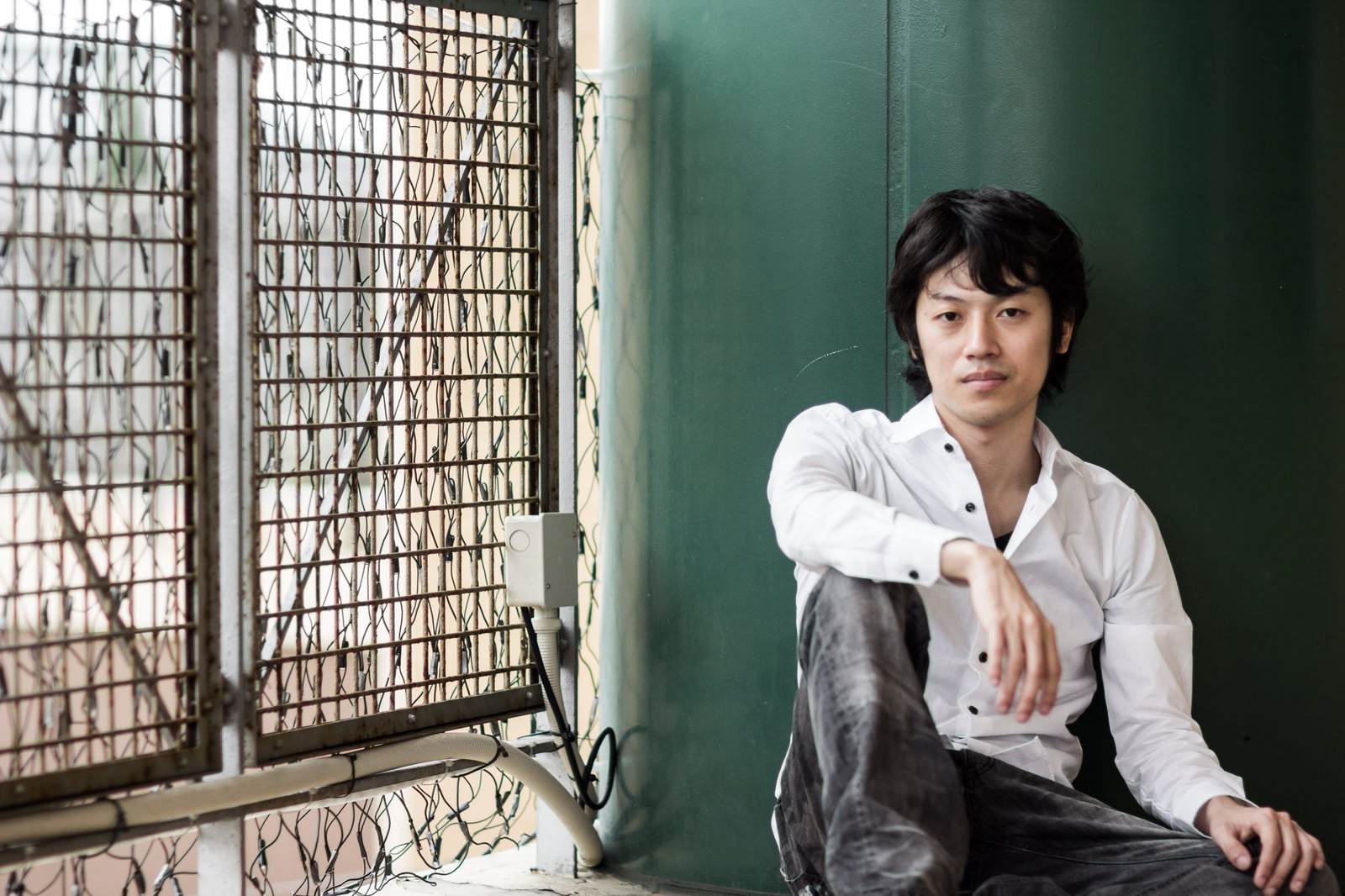 緑の壁に座り込む白シャツ姿の男性がジャケ写・メンナクポーズで横向きの悪い表情［モデル：Tsuyoshi.］