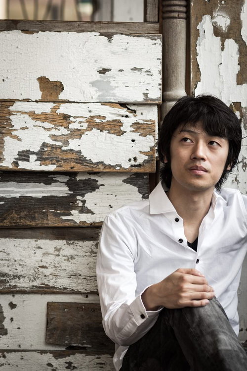 古い木壁を背にした表情の男性のジャケ写。切ない雰囲気のポートレート