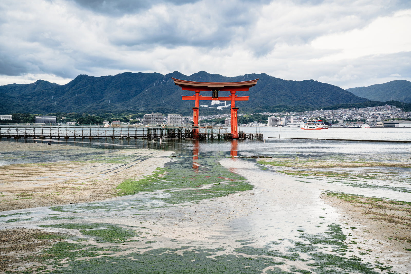 瀬戸内海に建つ厳島神社の朱色の大鳥居と広島の山並みの写真
