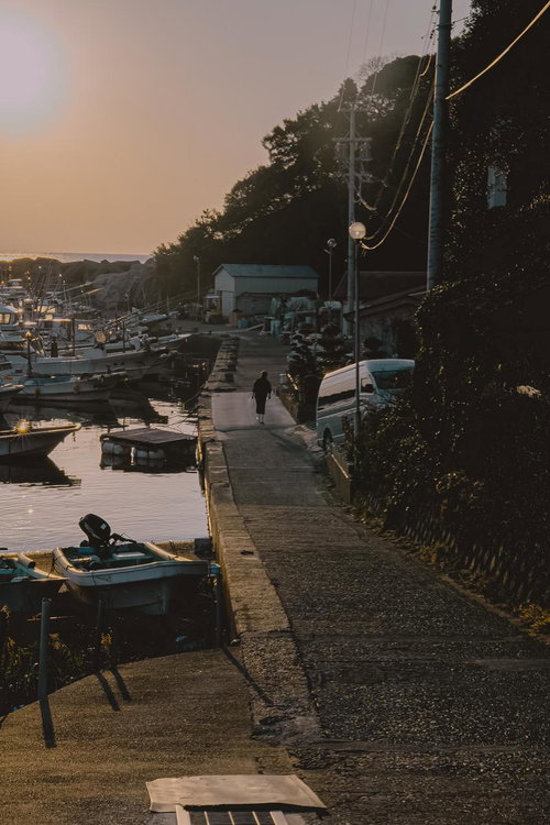 漁港の小道に差し込む朝日と帰路する住人の後ろ姿