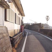 港町の裏通りにある赤い自販機と緩いカーブの道路の写真