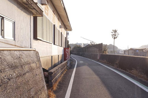 港町の裏通りにある赤い自販機と緩いカーブの道路